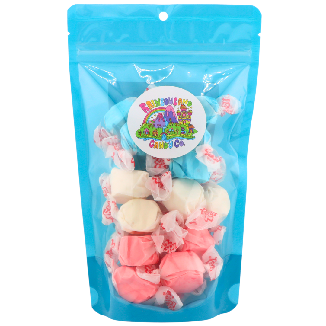 Blue resealable 6 oz RainbowLand Candy Co. bag of Stars & Stripes Taffy Trio featuring Salt Water Taffy pieces layered in red strawberry, white vanilla, and blue raspberry colors with the RainbowLand Candy Co. logo.