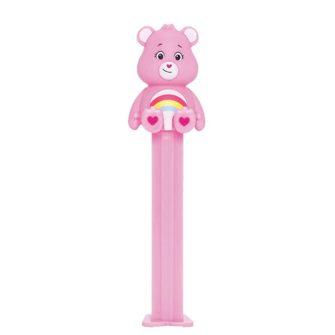 Pink Cheer Bear PEZ dispenser with a rainbow and heart belly badge, heart-shaped nose, and pink candy stem.