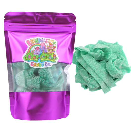 RainbowLand Candy Co. Green Apple Sour Belts in a purple metallic resealable stand-up pouch with a clear window, shown beside a loose pile of bright teal-green, sugar-coated green apple sour candy belts.