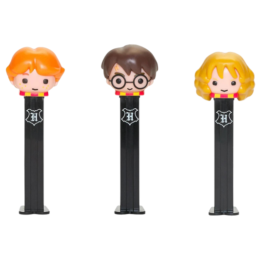 Three PEZ Harry Potter dispensers lined up together — Ron Weasley with orange hair, Harry Potter with round glasses and a lightning bolt scar, and Hermione Granger with curly blonde hair, each wearing a house scarf on a black dispenser with a Hogwarts crest.