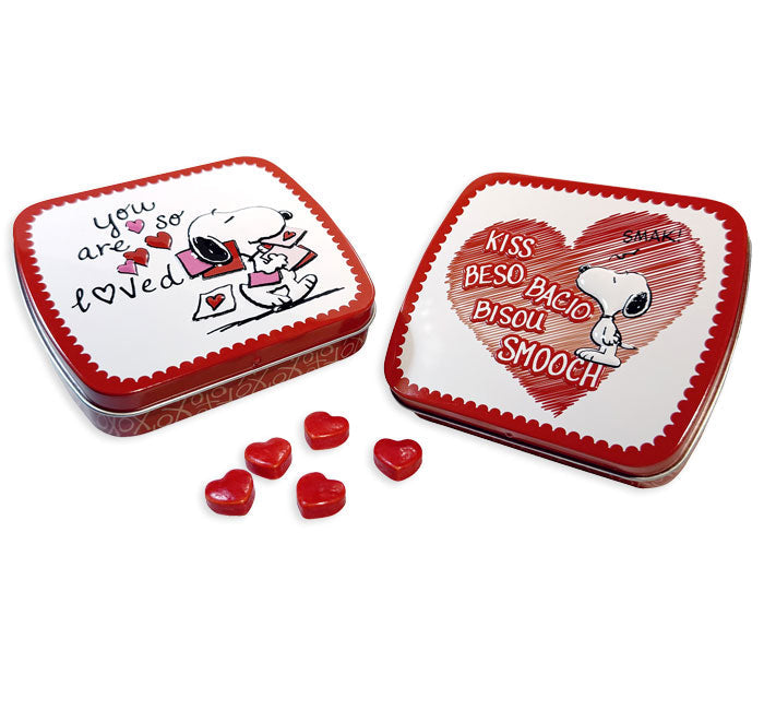 Peanuts Snoopy Valentine's Day candy tins, one open showing the "You Are So Loved" lid, one closed showing the "Kiss" heart design, five red heart-shaped strawberry candies beside the tins.
