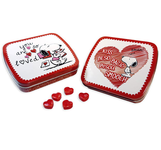 Peanuts Snoopy Valentine's Day candy tins, one open showing the "You Are So Loved" lid, one closed showing the "Kiss" heart design, five red heart-shaped strawberry candies beside the tins.
