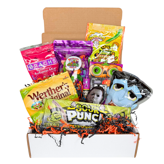 Halloween candy gift box with 10 spooky sweets nestled in orange and black paper shred, featuring a Sour Punch Frankenstein pack, Warheads Sour Caramel Apple chews, a Michael Myers candy tin, a cartoon vampire candy pouch, green pumpkin eyeball gummies, Werther's Caramel Apple Filled candy, Brach's Mellowcreme Autumn Mix, and a purple RainbowLand Candy Co. gummy pouch.